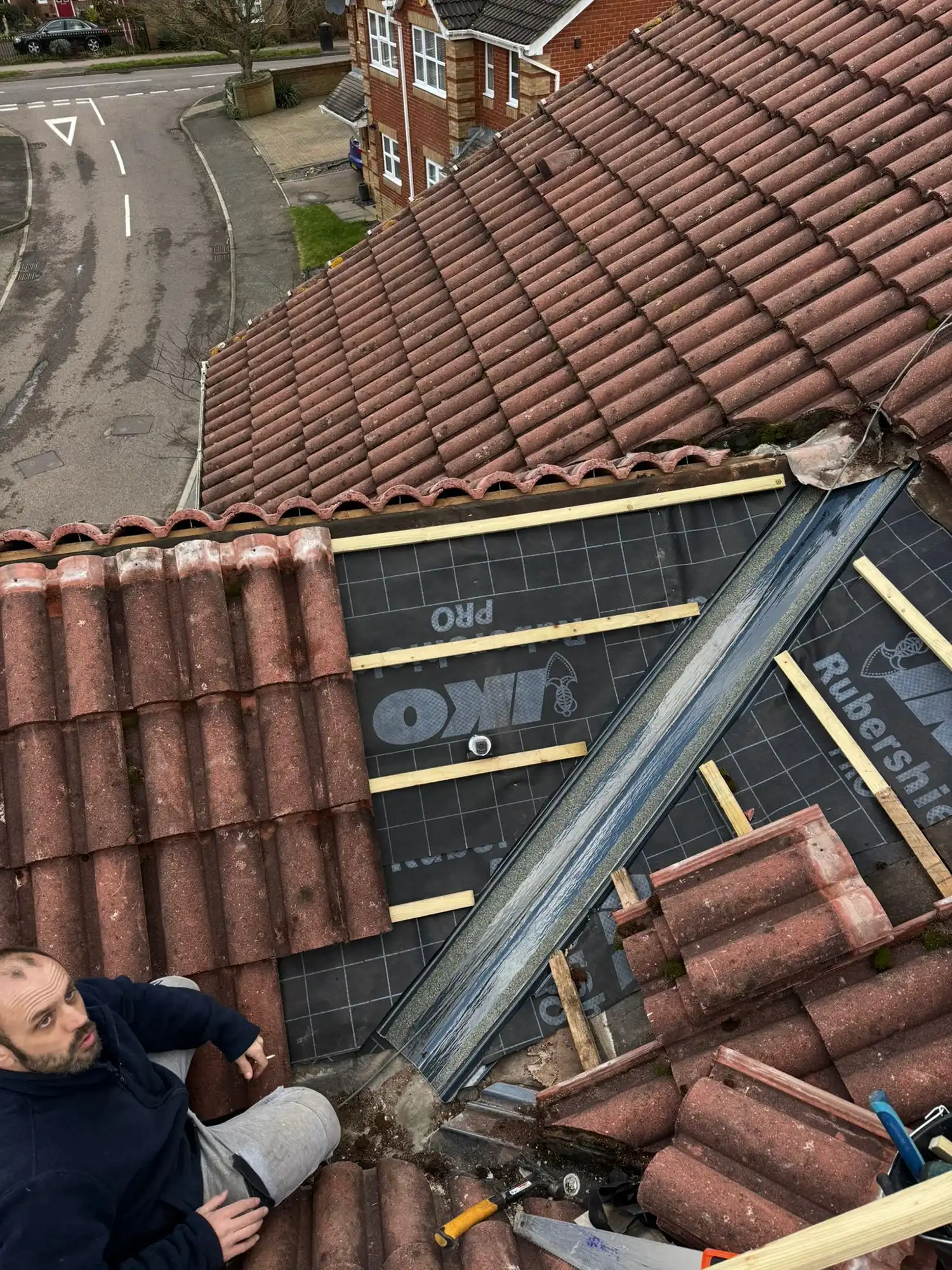 Man working on repairing a roof with red tiles and black waterproof underlay visible.