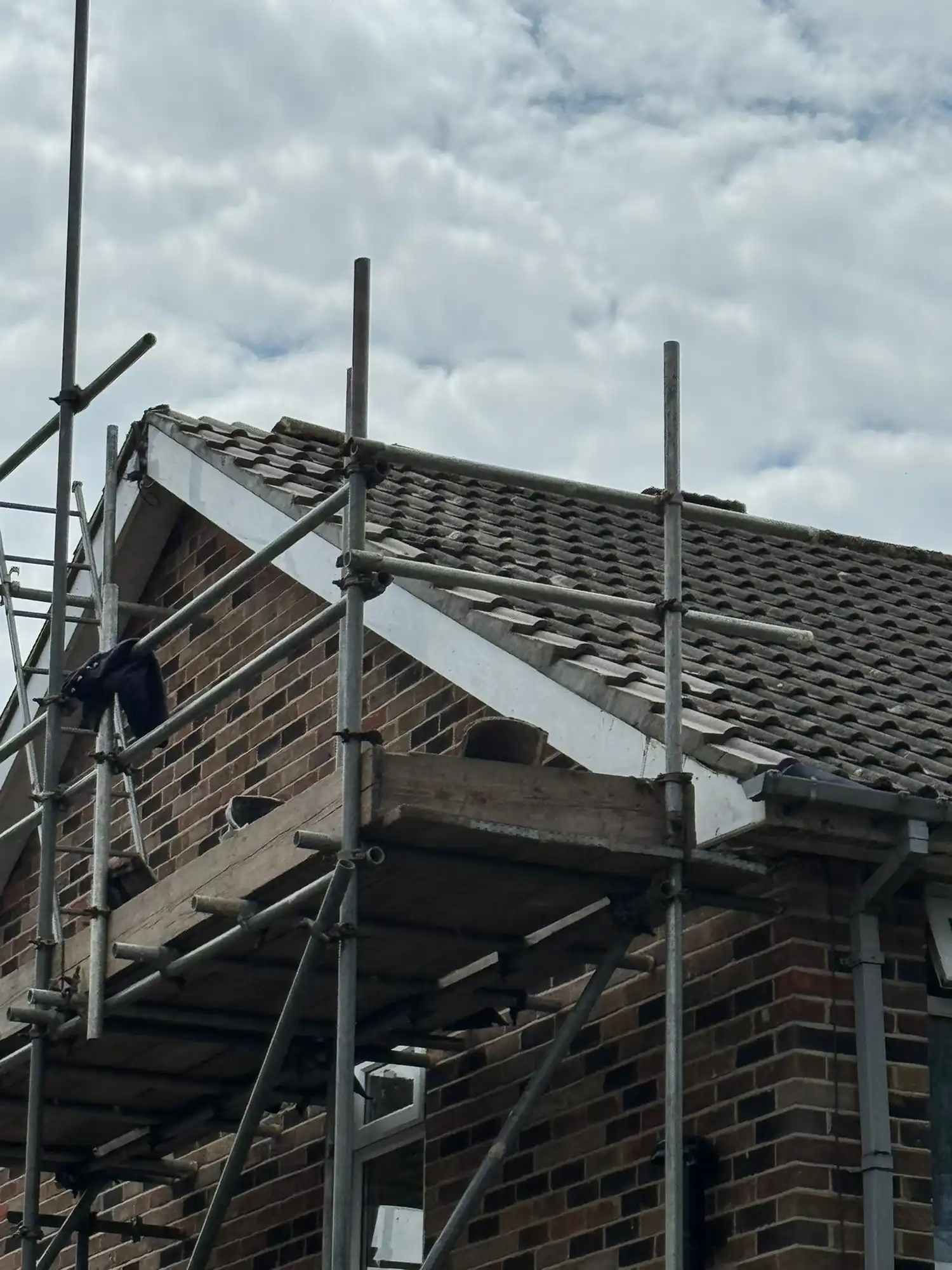 Brick house with tiled roof surrounded by metal scaffolding under a cloudy sky.