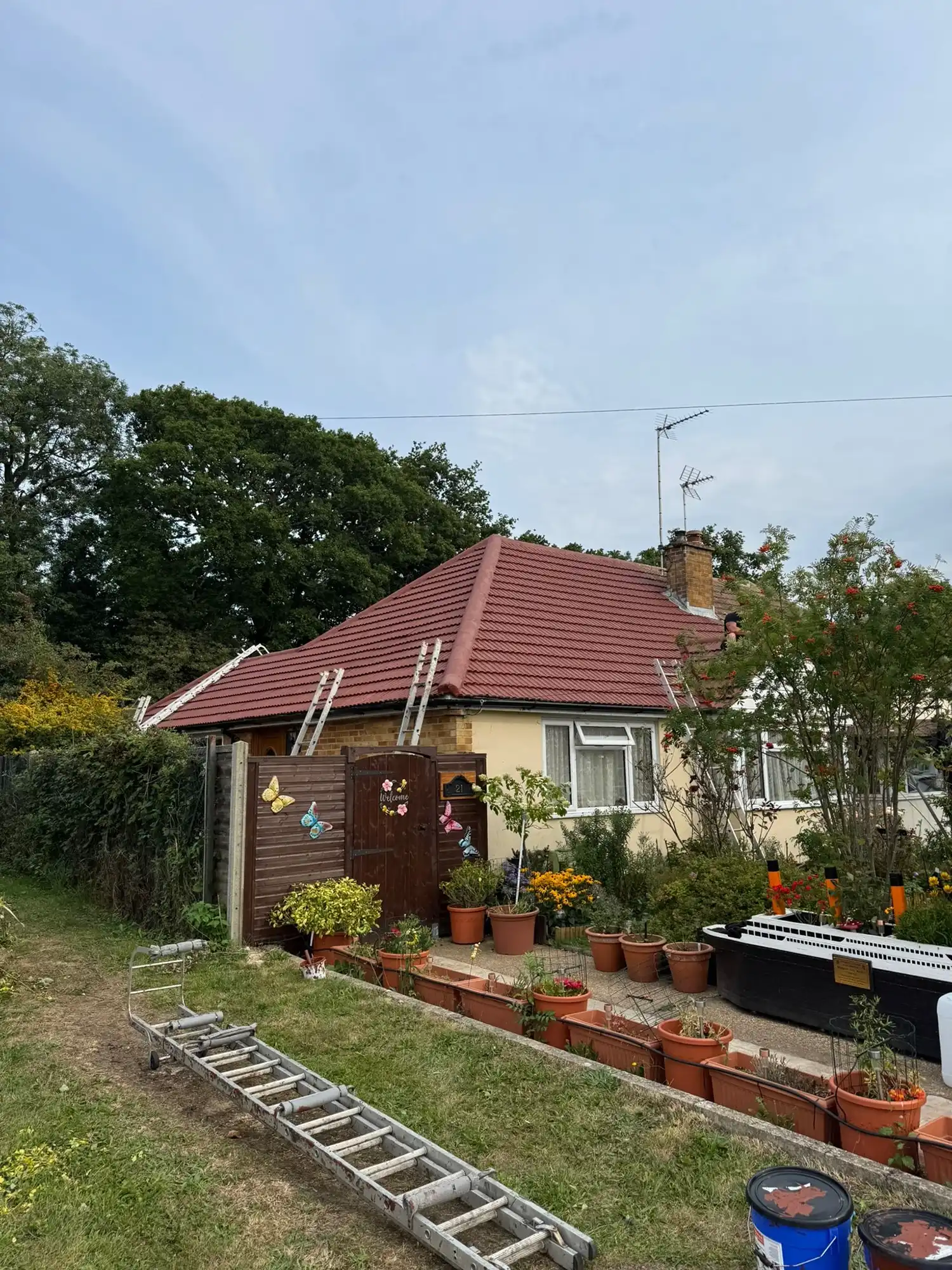 Single-story house with red roof and garden with potted plants and model ship outside.