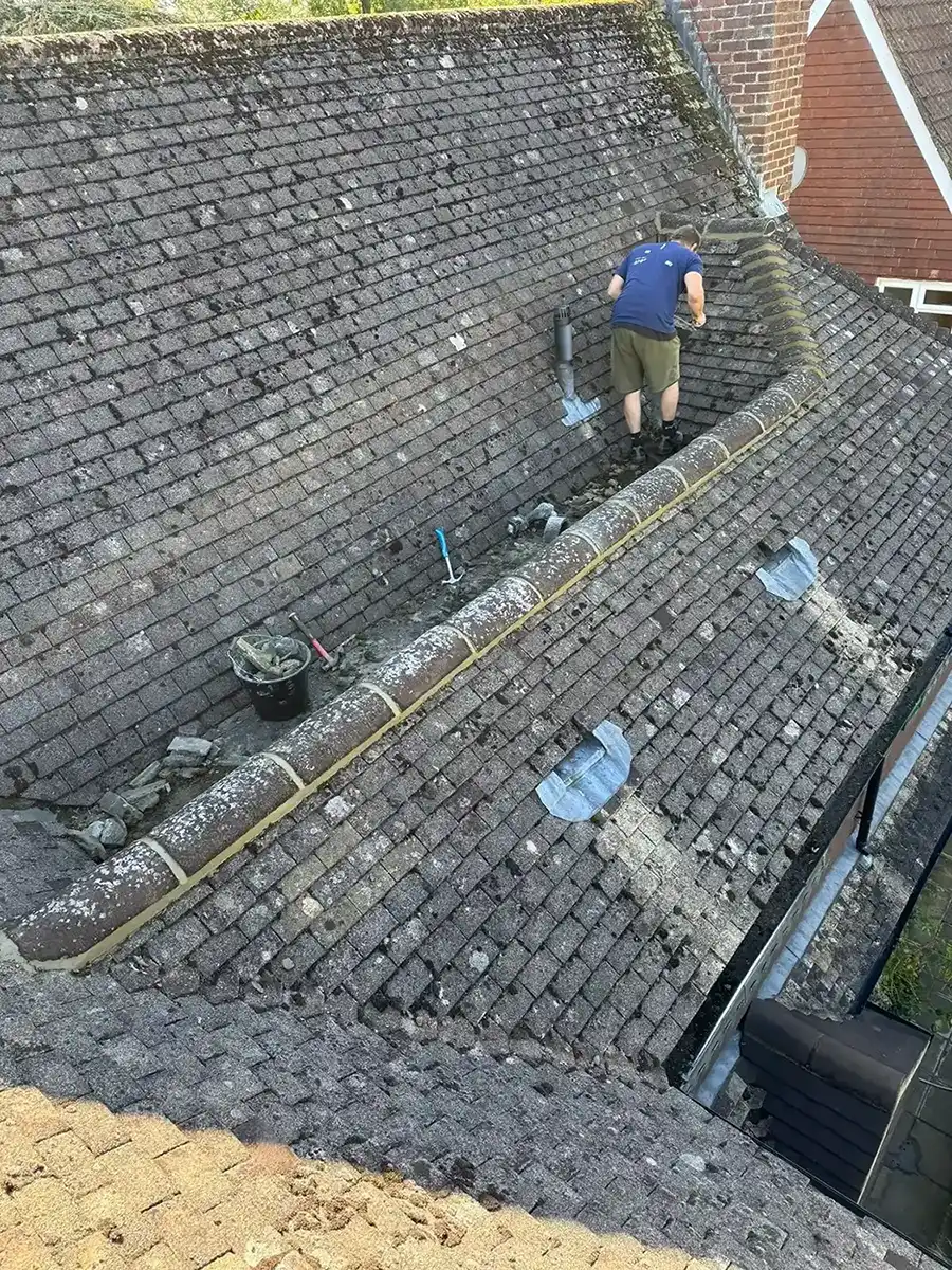 Person working on a mossy, weathered tile roof with tools and tiles placed nearby.