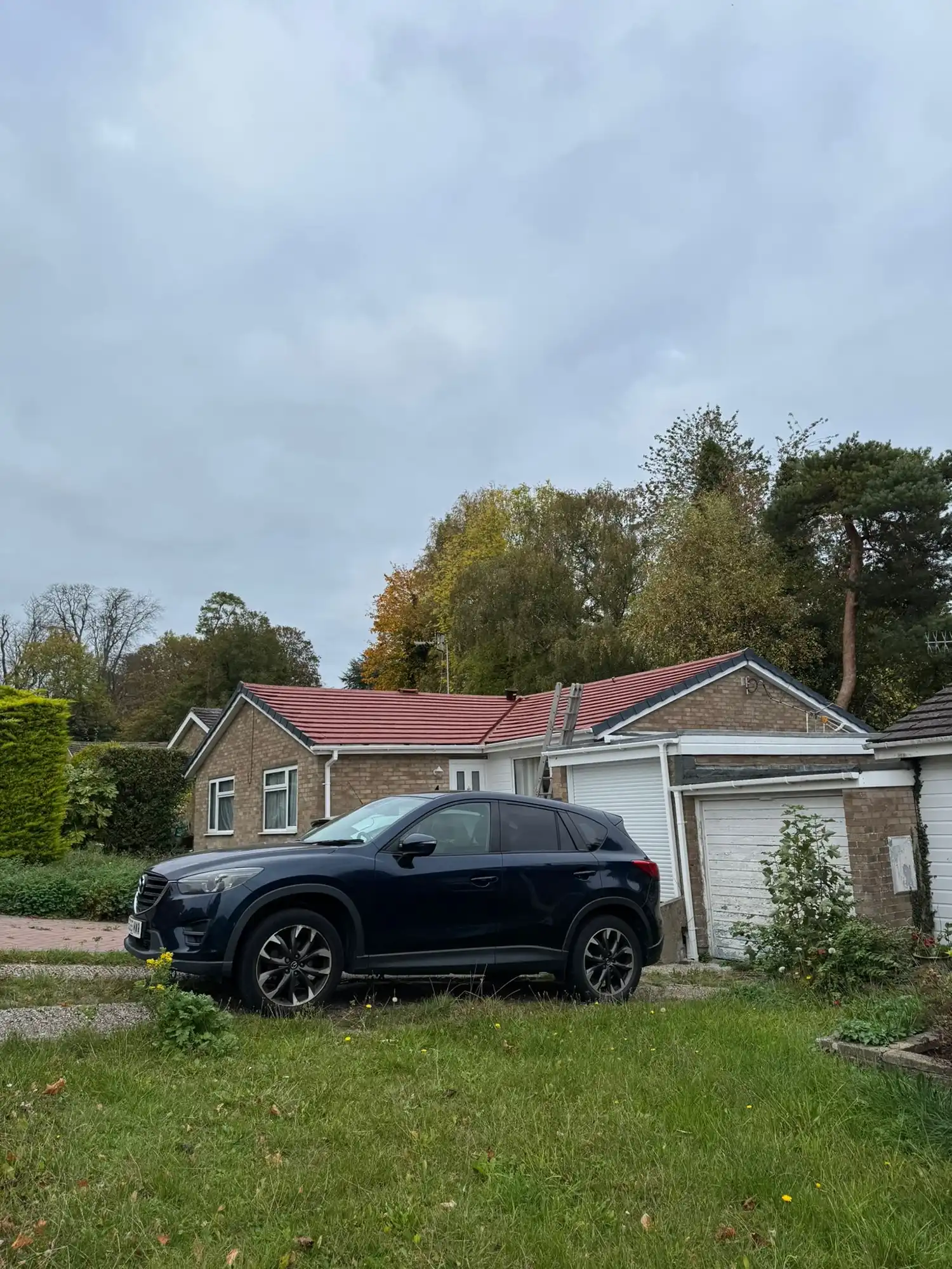Black SUV parked on a driveway beside a brick house with a red roof and garage doors.